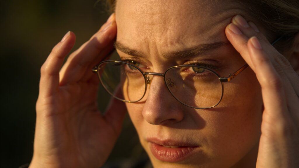 Mladá žena v brýlích si drží spánky, protože ji z nových brýlí bolí hlava.