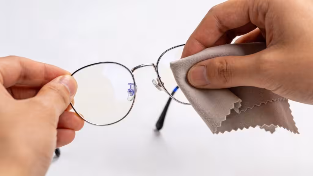 Ruce pečlivě čistí čočky dioptrických brýlí hadříkem z mikrovlákna.